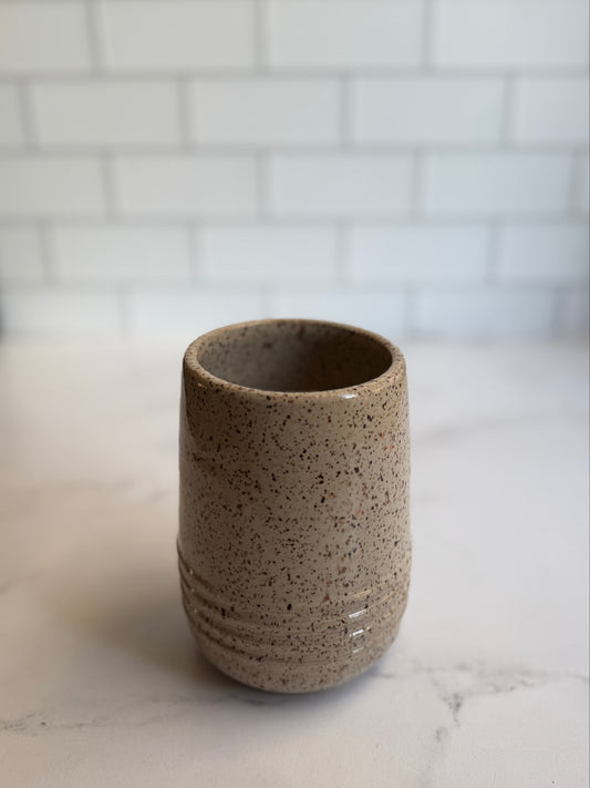 Speckled ceramic cup on a marble surface with a white tiled wall background